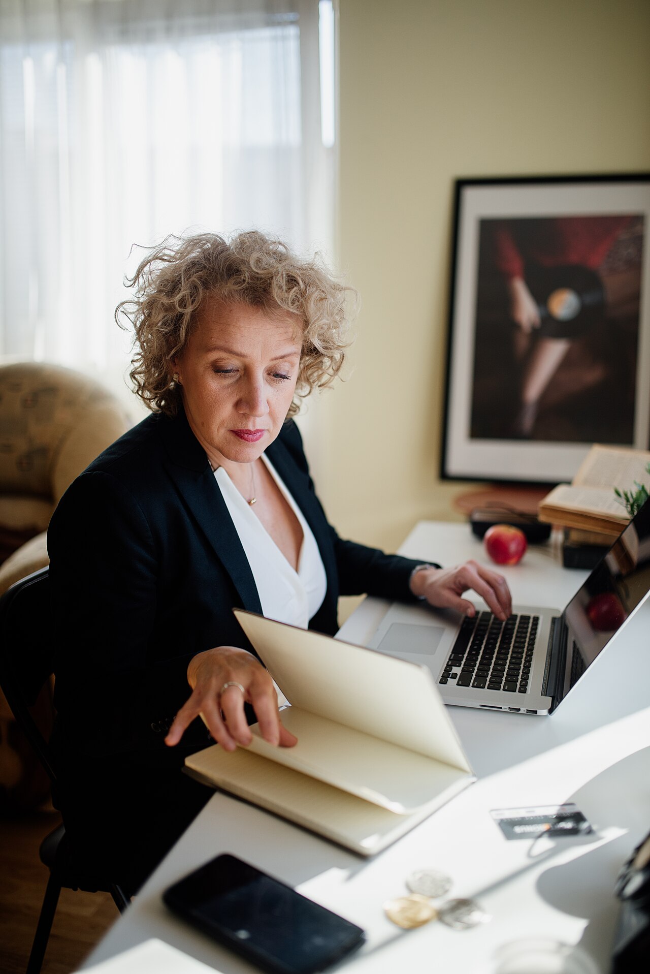 A worker at a desk in a bright office, working on a laptop with documents.